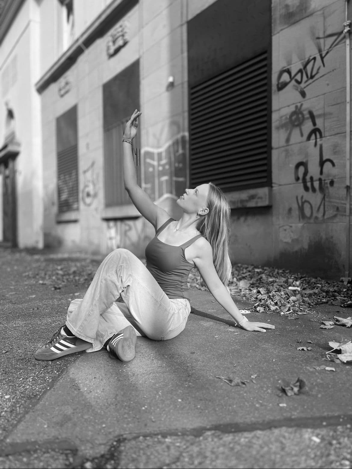 Frau tanzt im urbanen Umfeld vor einer grauen Wand mit Graffiti.